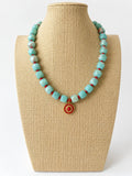 Aqua acrylic beaded necklace with small red beads and a red and gold-tone sun pendant on a beige jewelry bust.