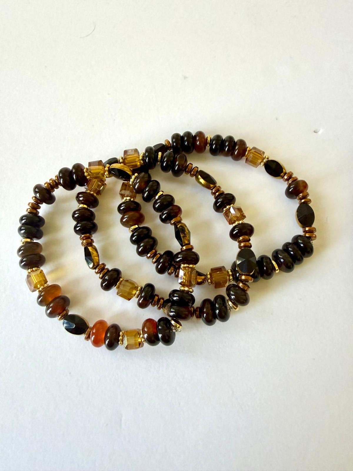 Three stretch bracelets with glossy brown and black beads, amber-colored faceted crystals, and gold-tone daisy spacers on a white background.