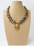 Necklace with elongated beige and black spotted beads, small gold-tone spacers, and an oval gold-tone sunburst pendant.
