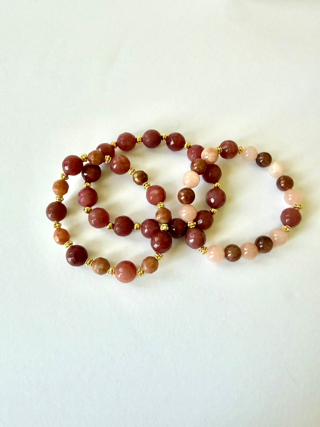 Set of three faceted agate beaded bracelets in burgundy, brown, and peach tones with small gold-tone spacers on a white background.