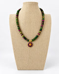 Green and purple jade beaded necklace with gold-tone accents and a round purple pendant with an orange center on a beige jewelry bust.