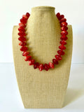 Red acrylic beaded necklace with rounded oval beads and pale marbled swirls on a beige jewelry bust.