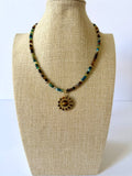 Multicolor faceted crystal beaded necklace with a round gold-tone pendant featuring a simulated tiger's eye focal stone on a beige jewelry bust.