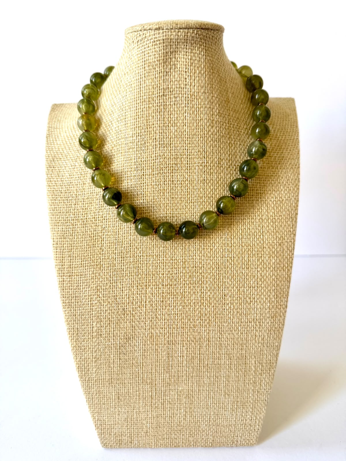 Olive green acrylic beaded necklace with rounded marbled beads and small gold-tone spacers on a beige jewelry bust.